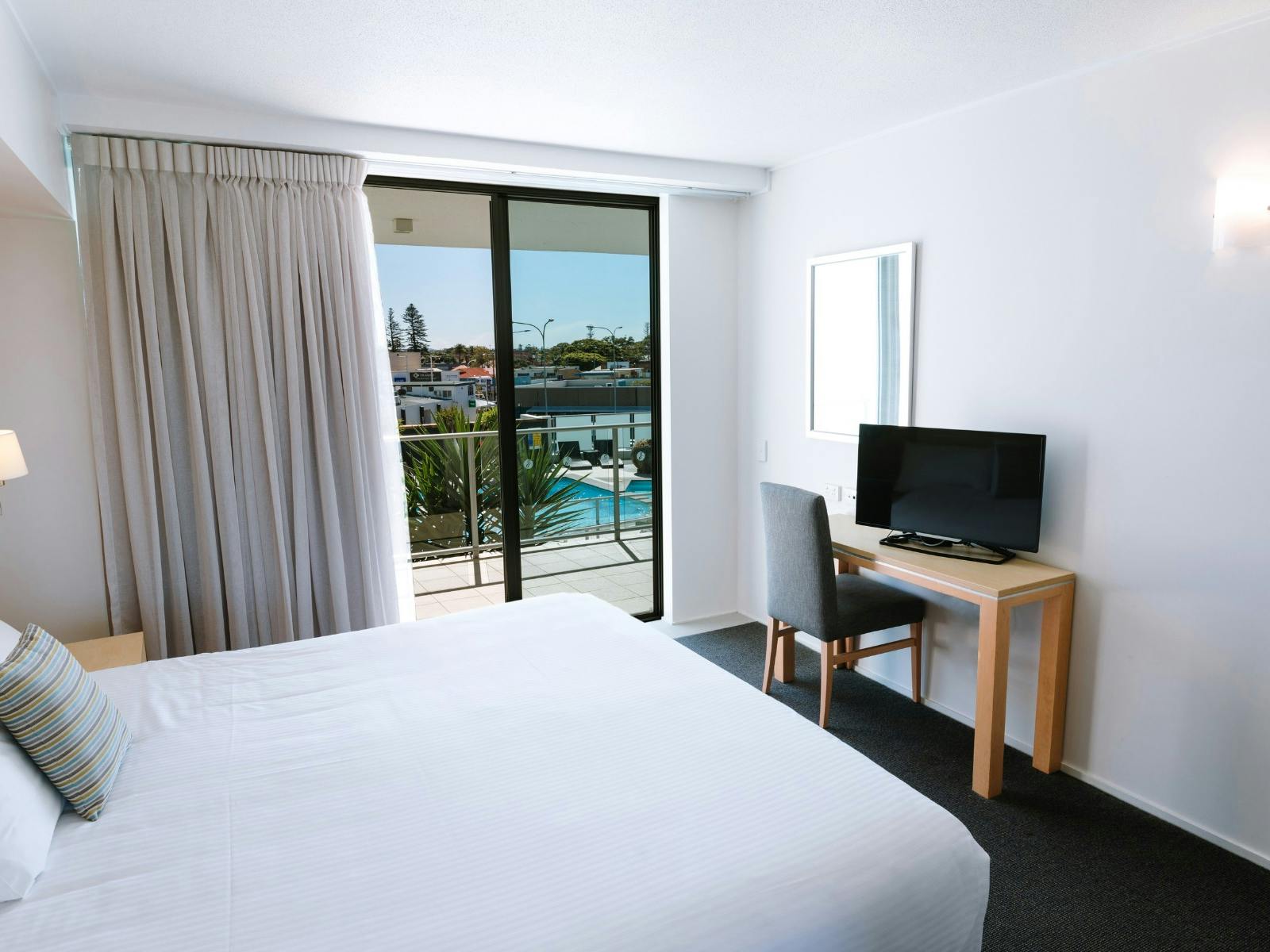 Picture bed facing a desk and television. A pool can be seen from outside.