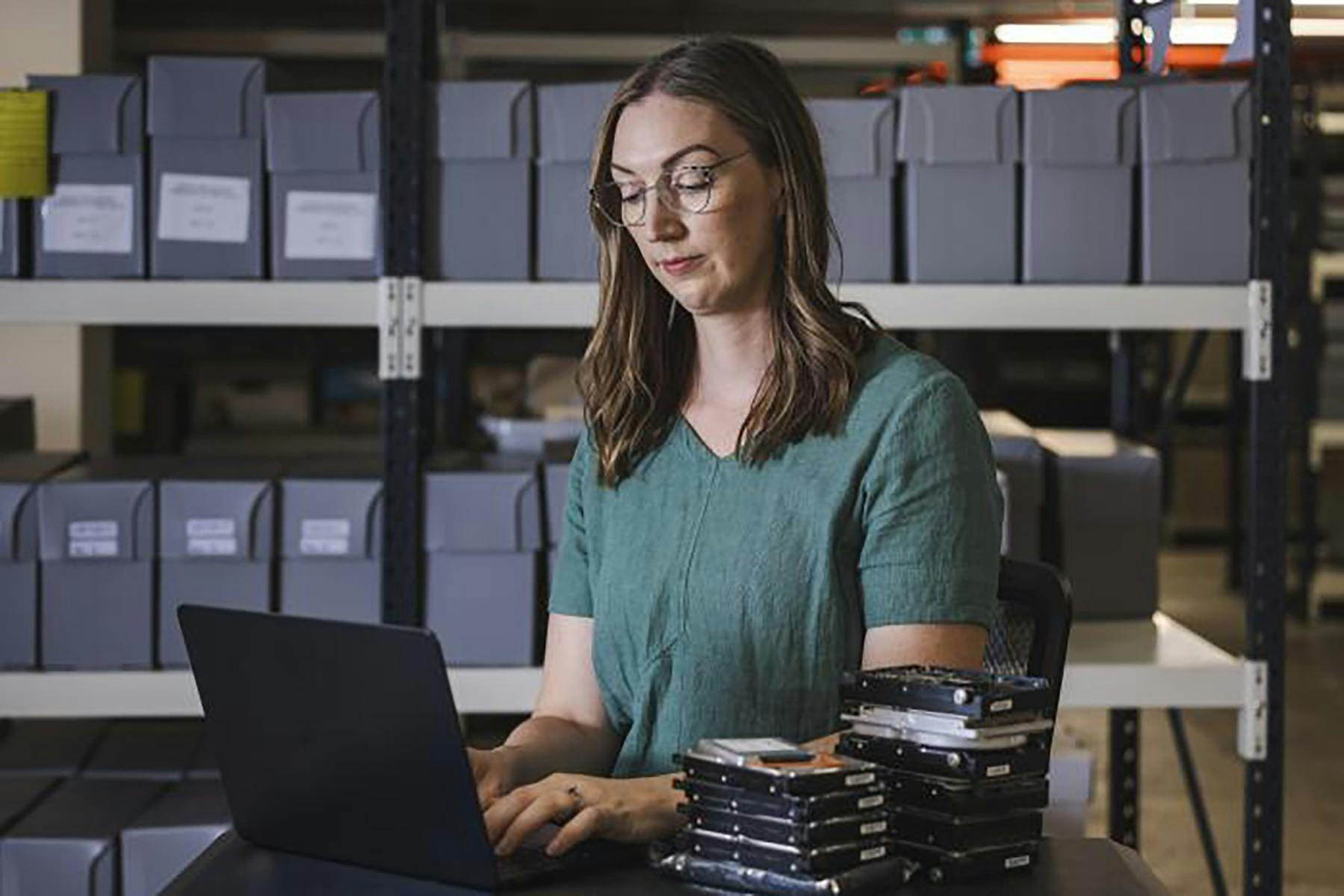 A woman working at a laptop in a room with boxes of records