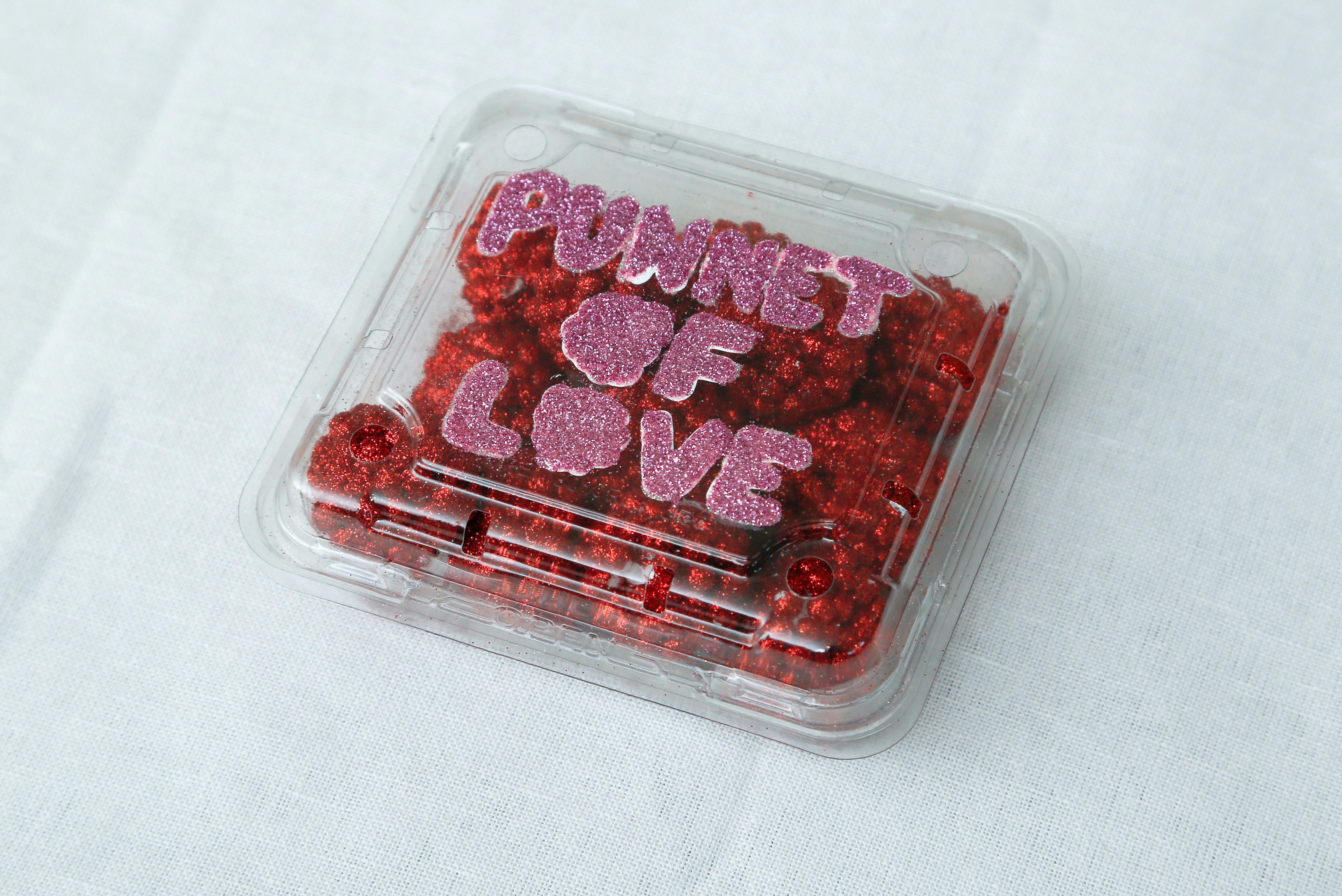 Small red raspberry sculputred in a plastic punnet with bubble pink letters spelling 'Punnet of Love