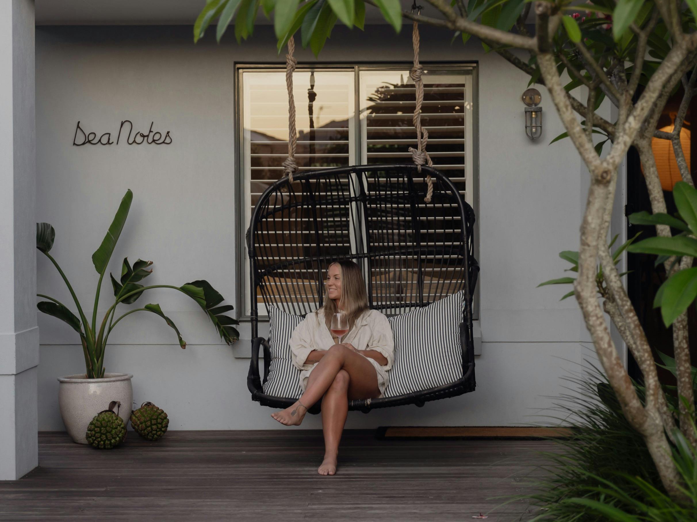 female guest enjoying a glass of wine in hanging chair on verandah