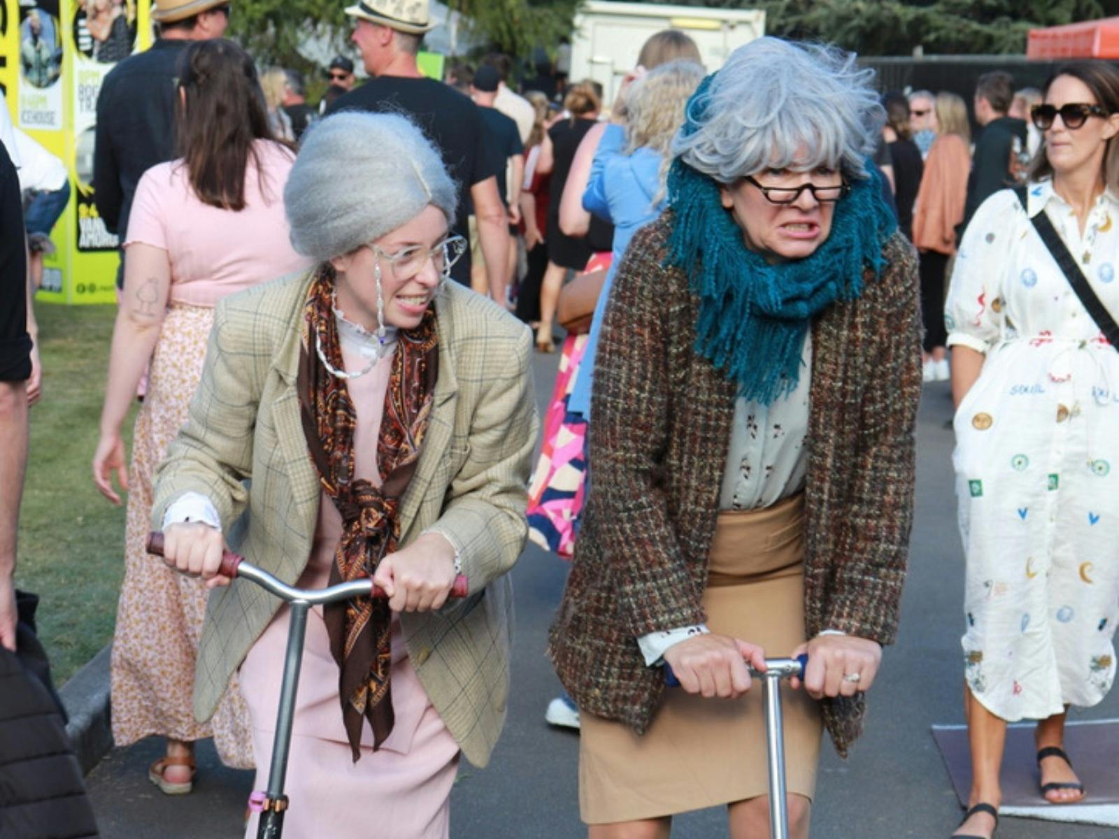 Two women dressed as grannies on scooters