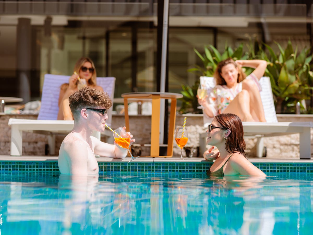 Group of friends enjoining drinks by the pool and in the pool at Hibiscus Bar & Terrace
