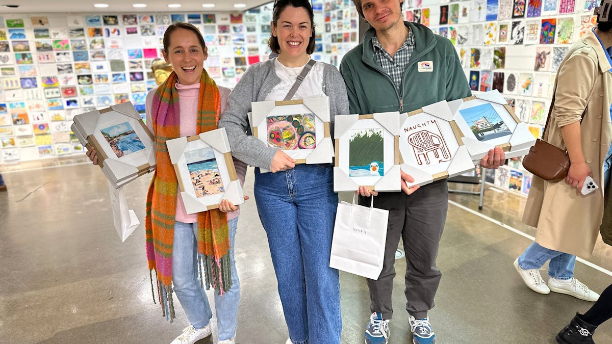 Three people holding framed A5 original artworks they bought at the Incognito Art Show.