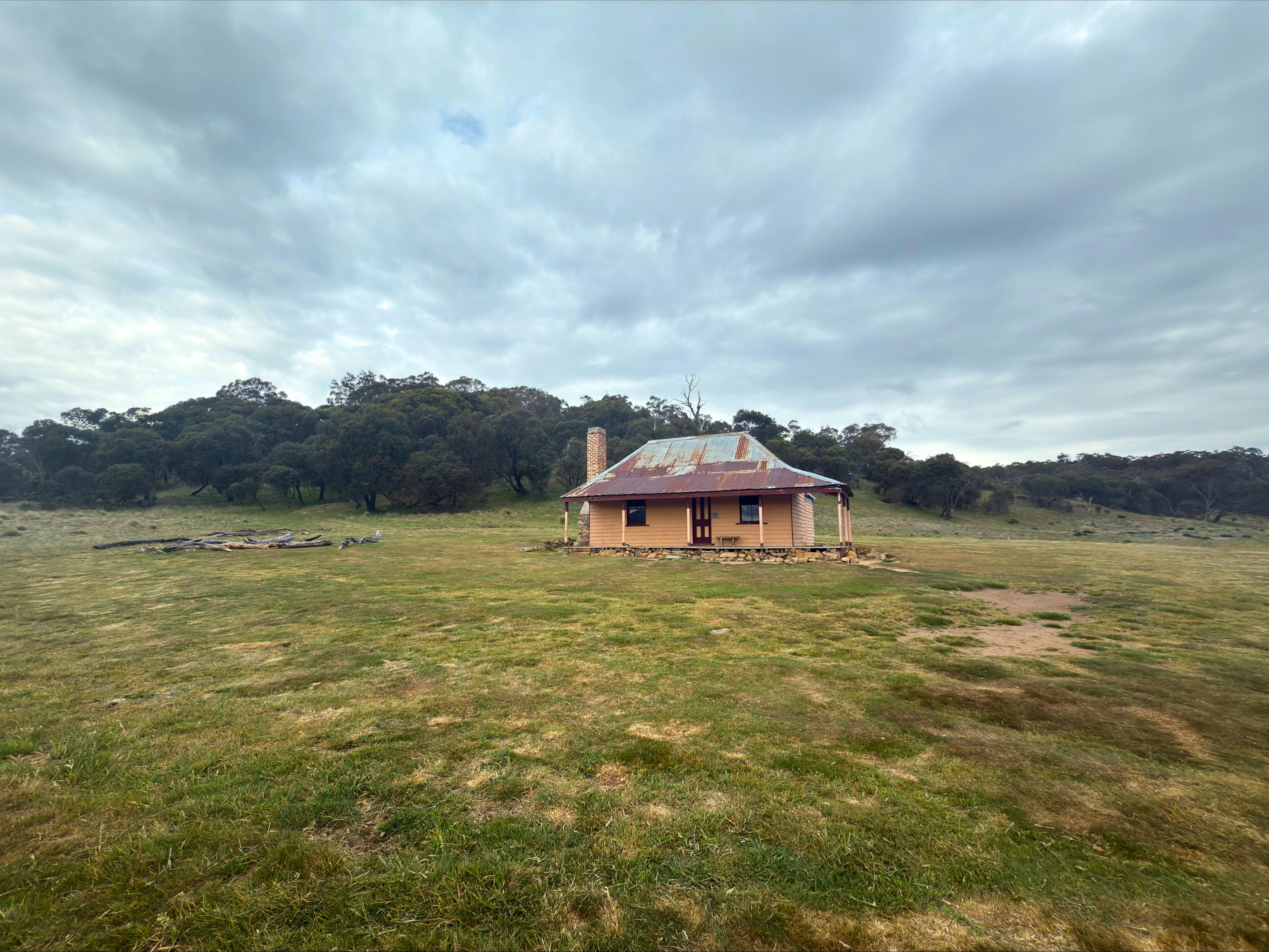 A hut in open terrain with trees in the background and an overcast sky.