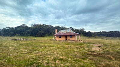 A hut in open terrain with trees in the background and an overcast sky.