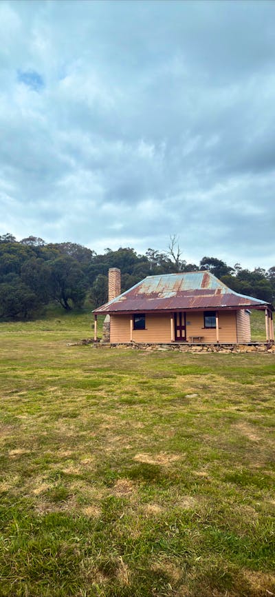 A hut in open terrain with trees in the background and an overcast sky.