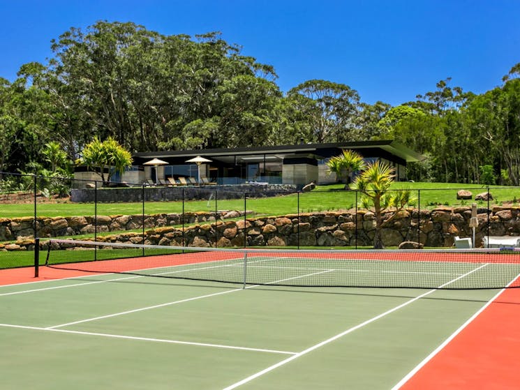 Large entertaining area featuring a tennis court, surrounded by seating and lush greenery