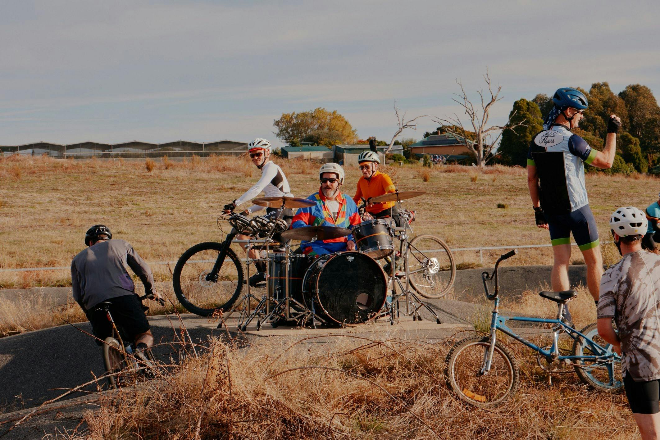Drummer playing music surrounded by BMX and Mountain bike riders on a course.