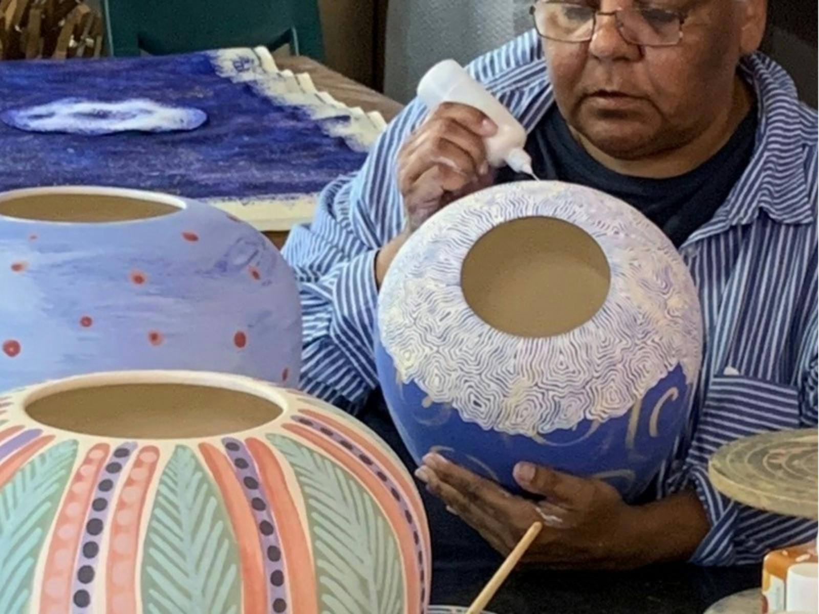 Artist meticulously painting intricate designs on pottery in vibrant pastel colors.