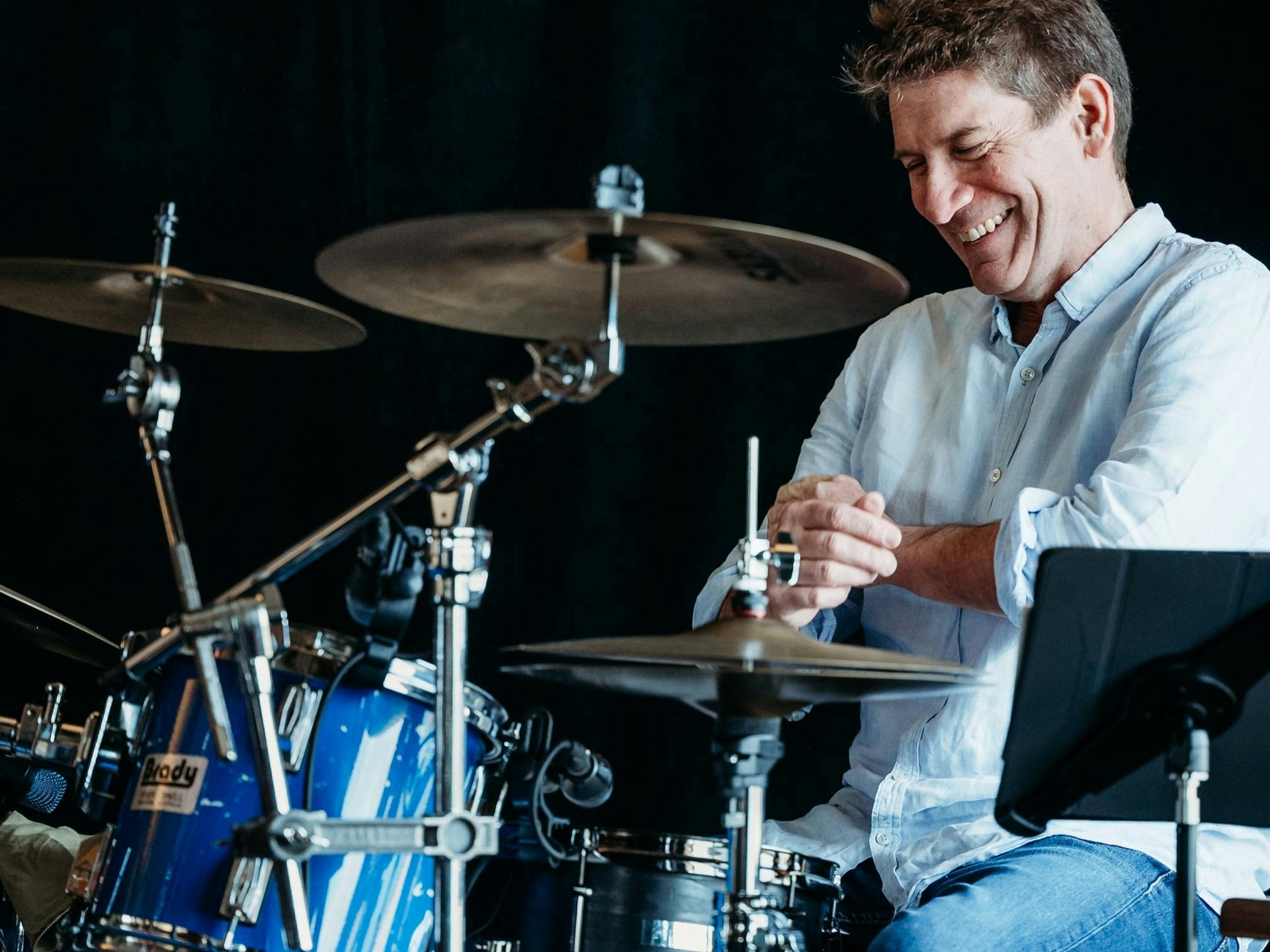 A man seated at a drum kit, leaning back and smiling.