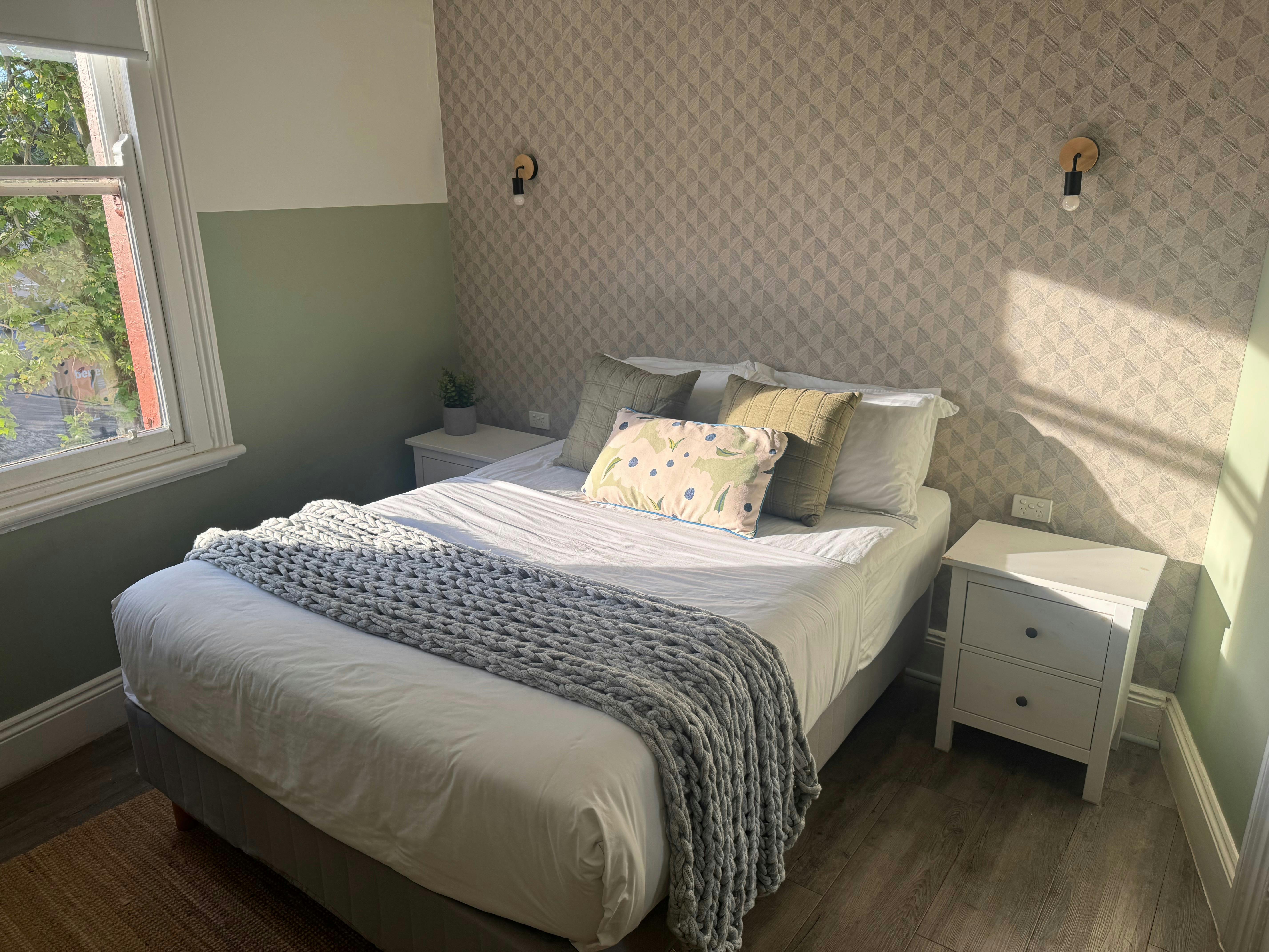 Sunlit guest room at Native Rose Hotel with a queen bed, bedside tables, window and soft green and n