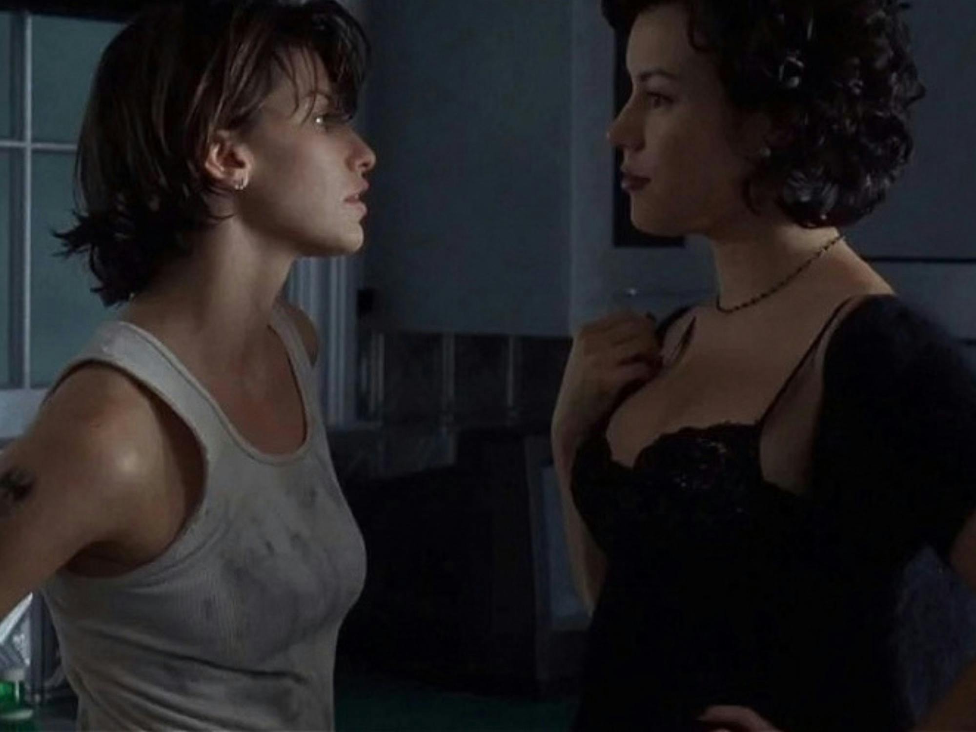 Still with Gina Gershon Jennifer Tilly standing face to face in a dim bathroom with a charged look