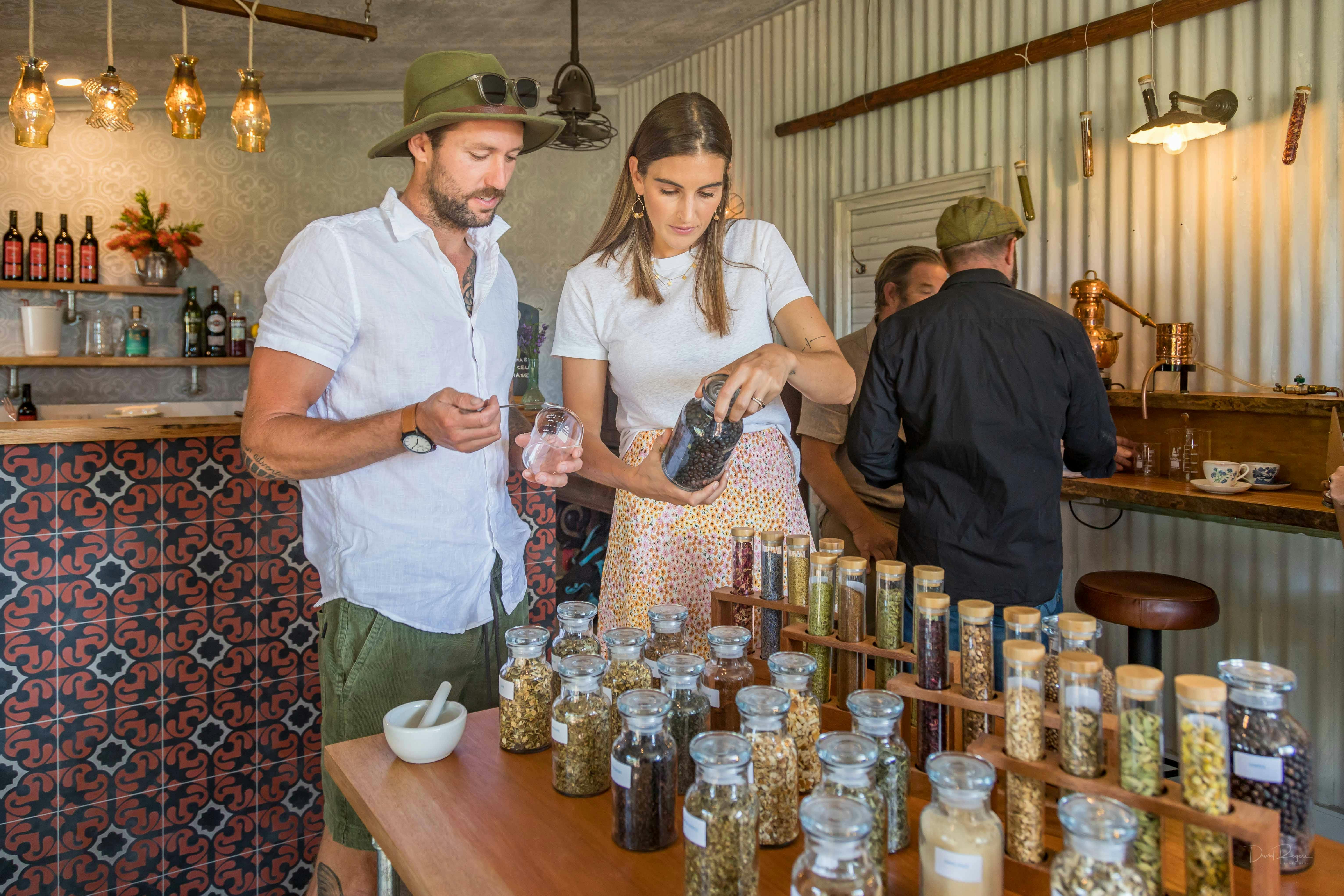 Man and woman at table. Table has jars and test tubes full of different types of botanicals.