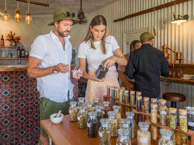Man and woman at table. Table has jars and test tubes full of different types of botanicals.