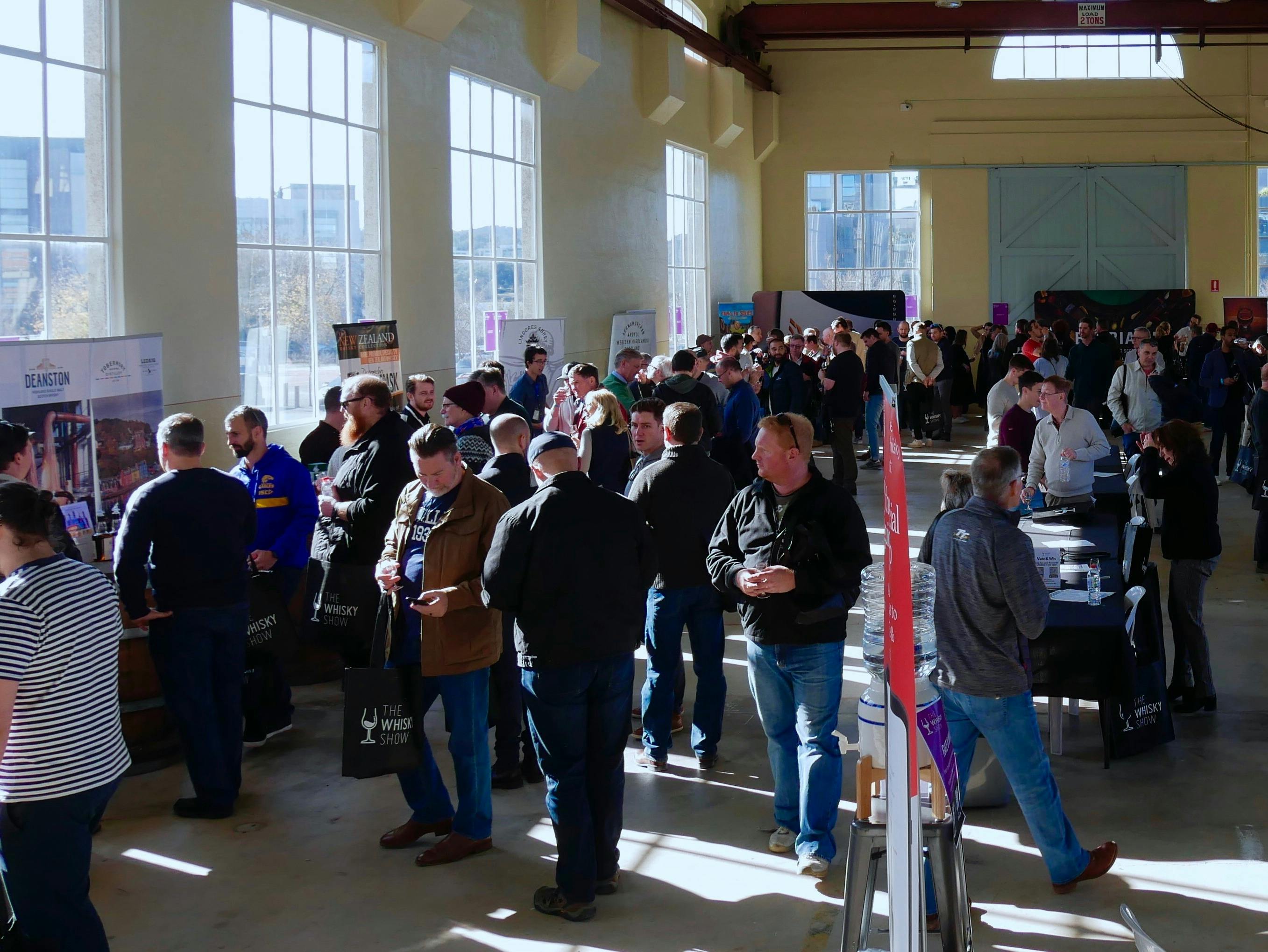 crowd of people inside a large, well lit warehouse tasting whiskies.