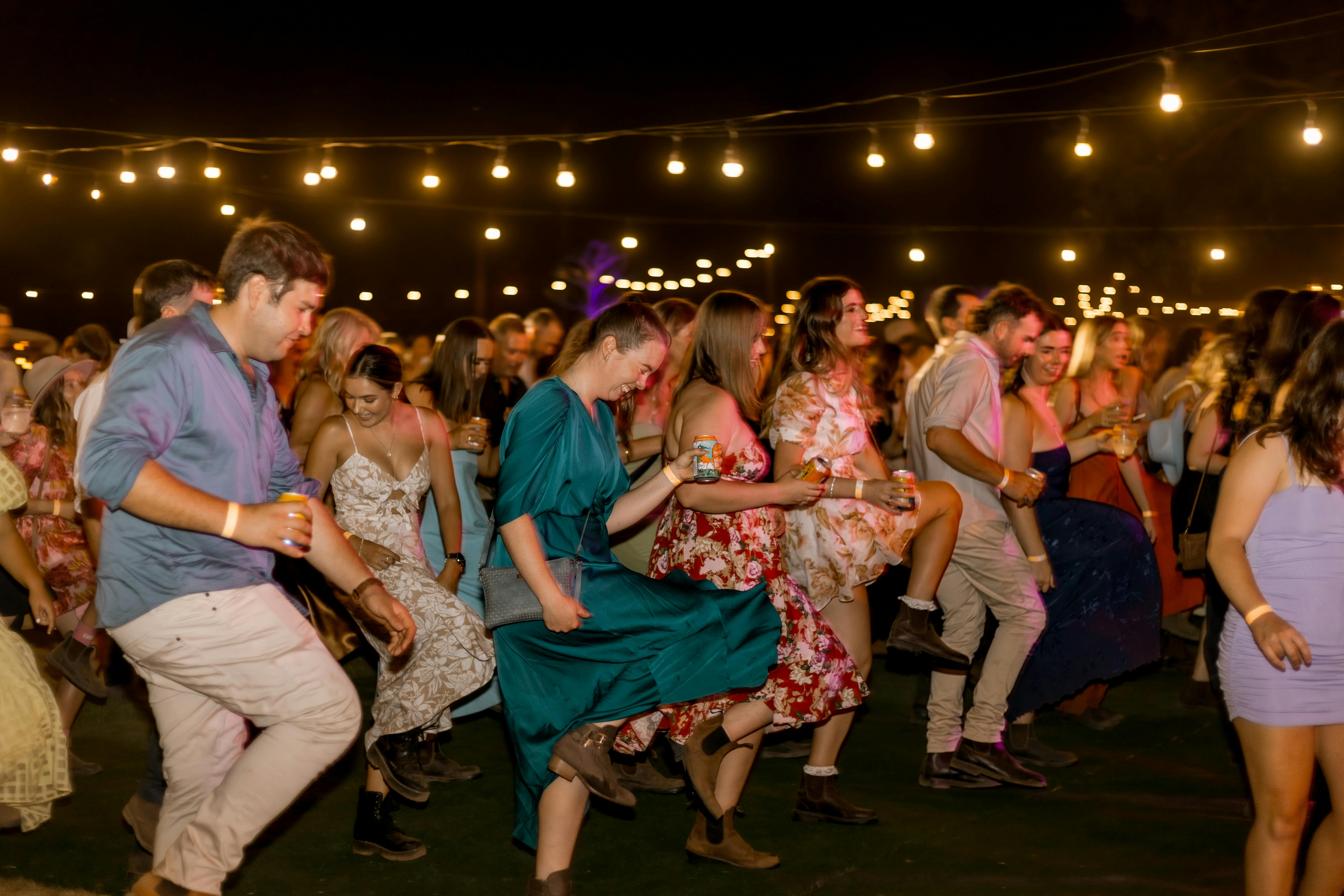 Dance floor filled with young adults line dancing under festoon lights