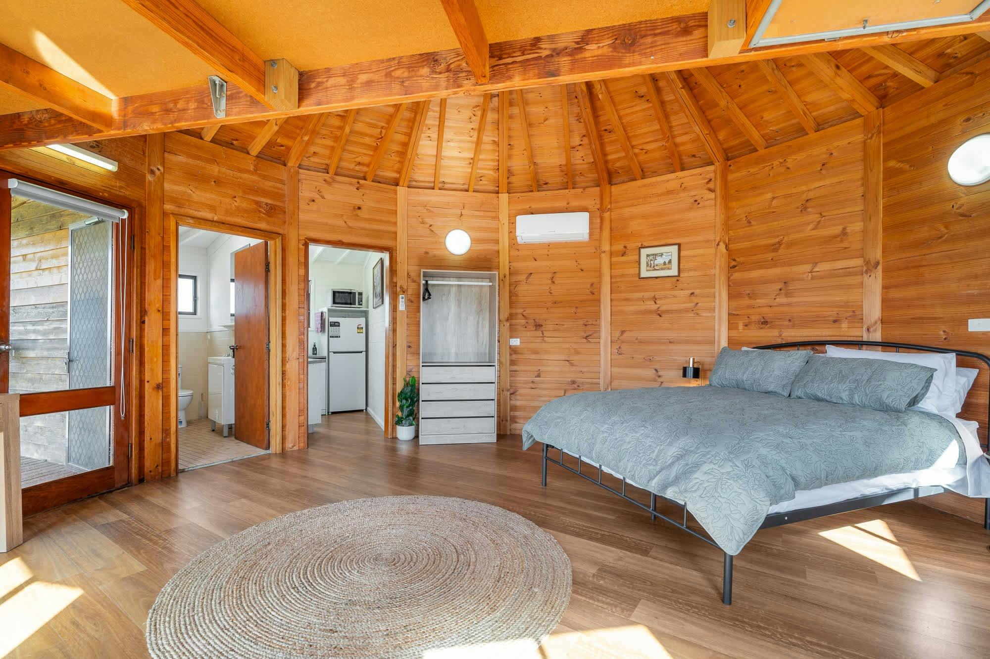 회색 침구가 깔린 퀸 사이즈 침대 열린 옷걸이 공간 욕실 주방 외부로 이어지는 문