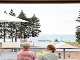Two guests seated on the balcony overlooking Robeu2019s foreshore and sea.