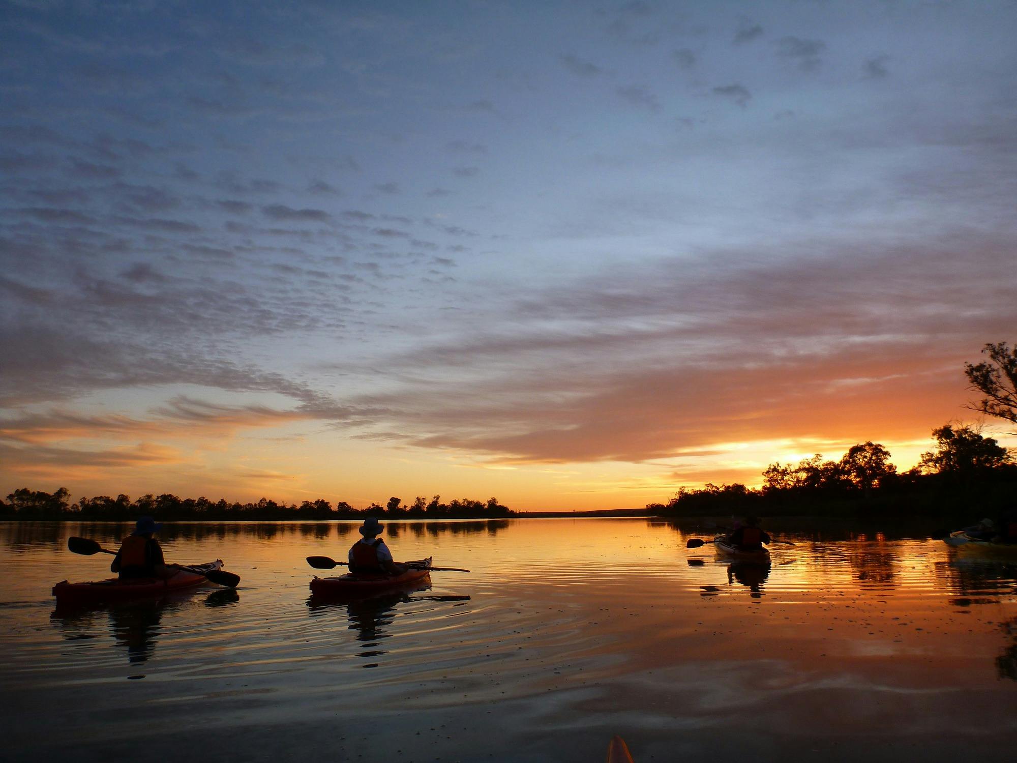 kayakers floating on the river with a lovely sunset in the sky and reflected on the water.