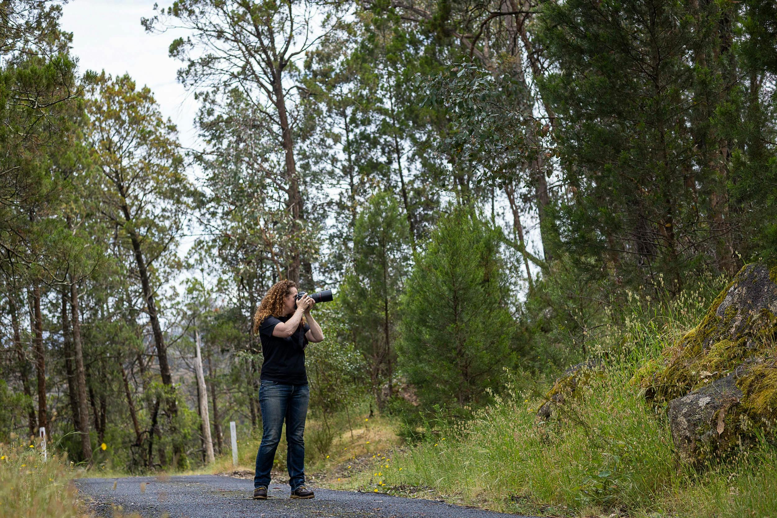 Woman standing with camera taking photos of trees in a park