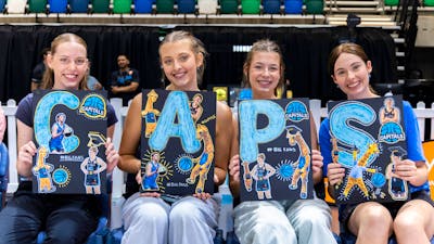 UC Capitals fans smiling while sitting courtside with posters of the athletes.