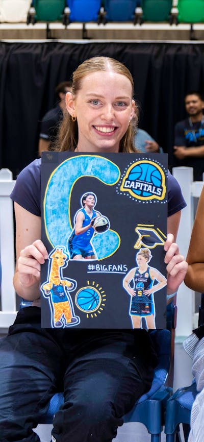 UC Capitals fans smiling while sitting courtside with posters of the athletes.