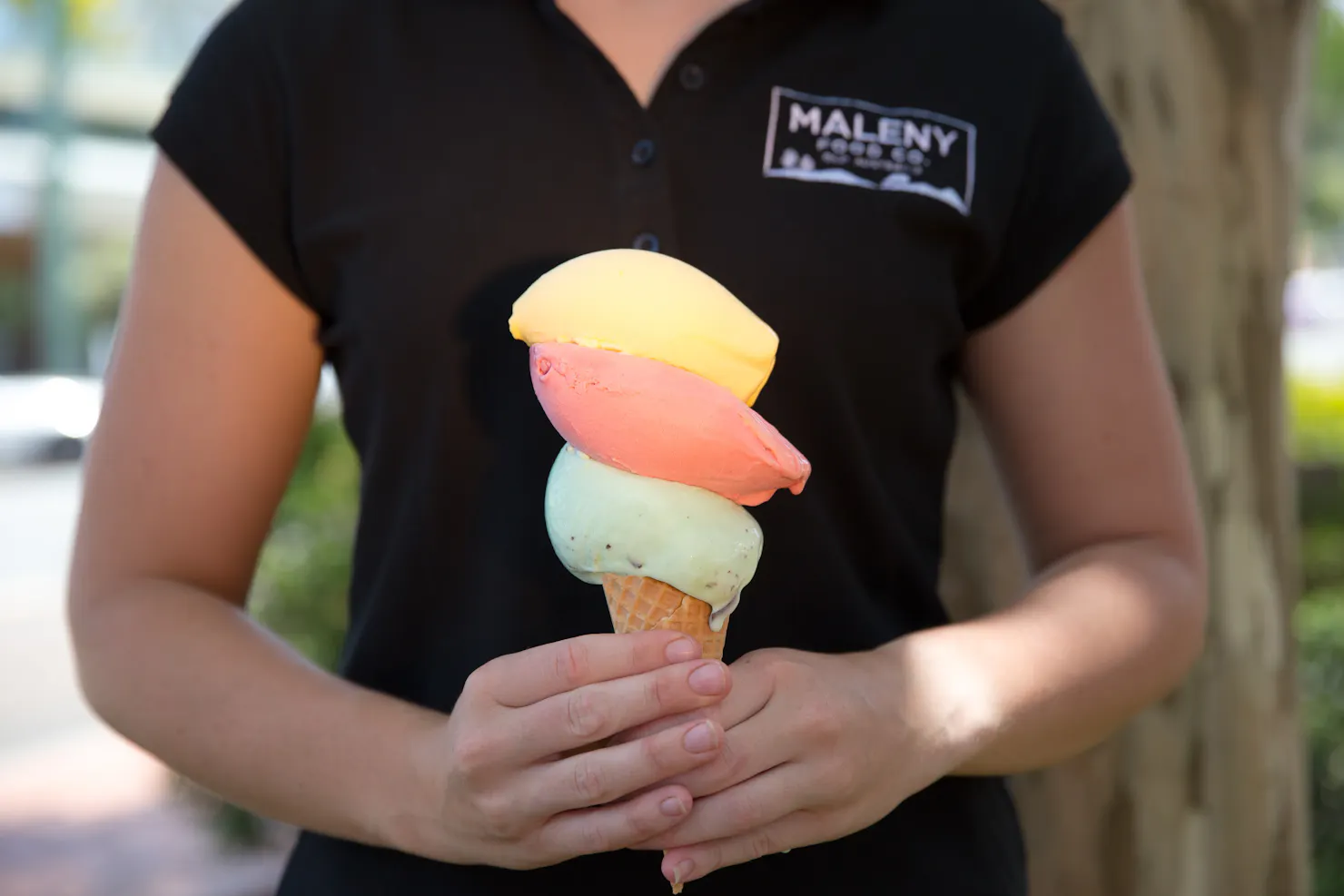 Lady holding a gelato in a cone with 3 huge scoops of gelato.