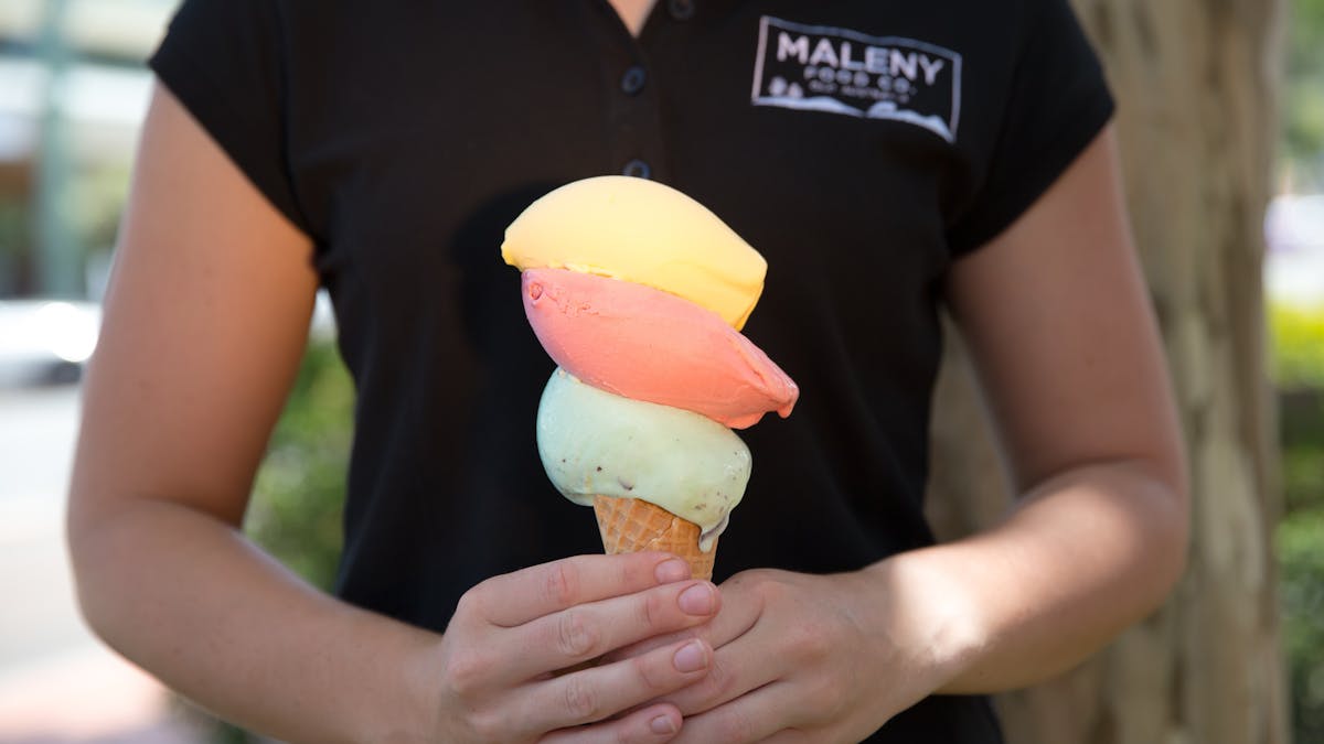 Lady holding a gelato in a cone with 3 huge scoops of gelato.