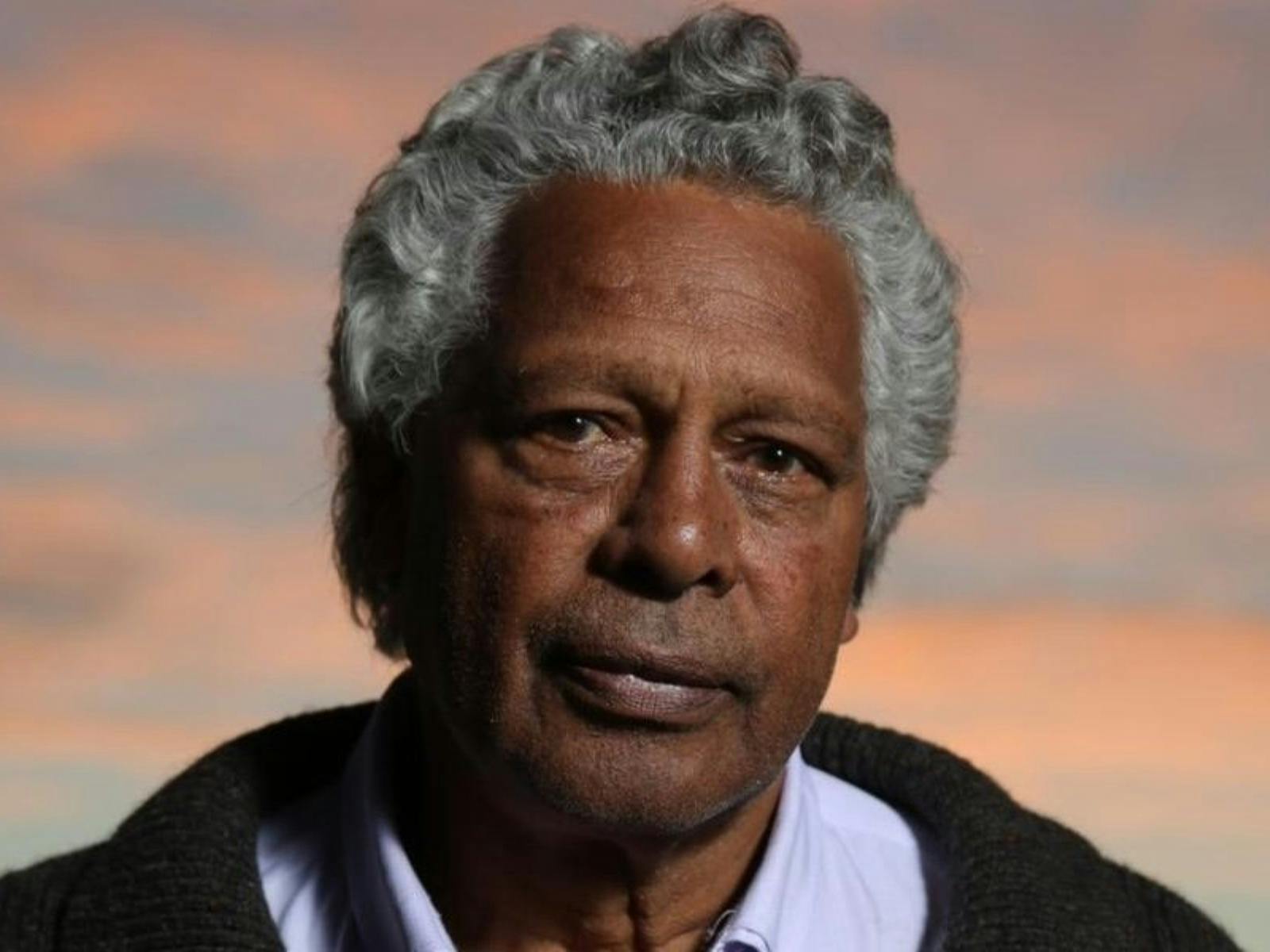 Close-up of Ernie Dingo looking directly at the camera against a sunset sky
