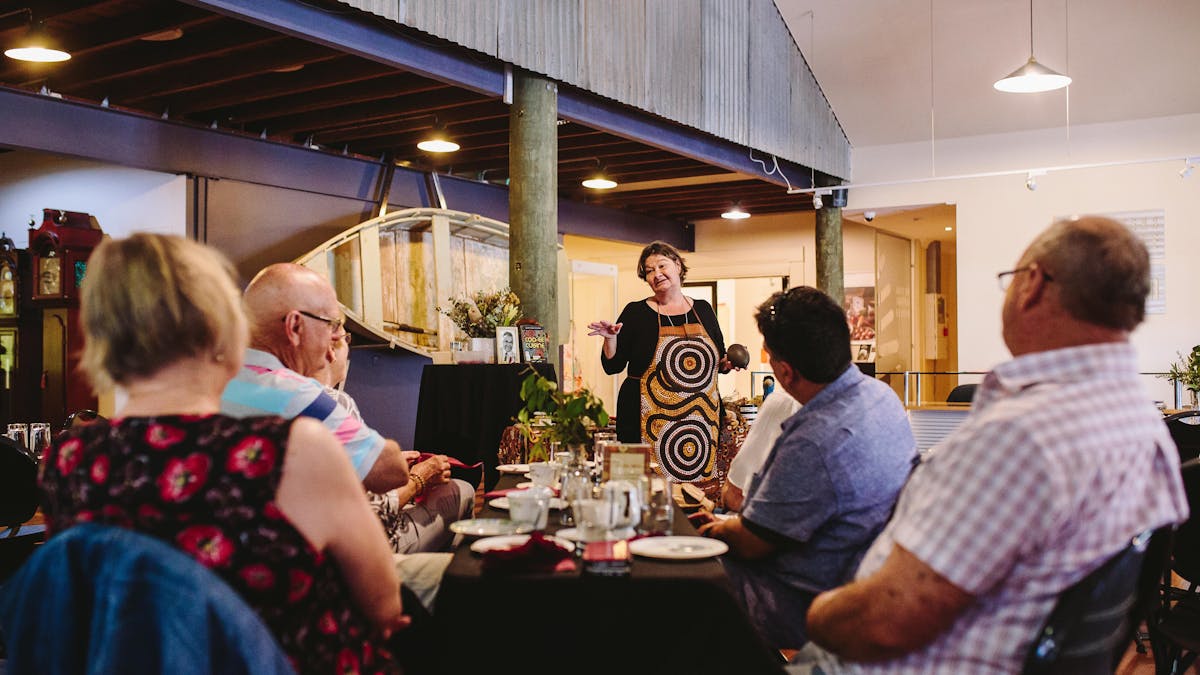 Lady talks to a group of adults that are sitting around a dining table