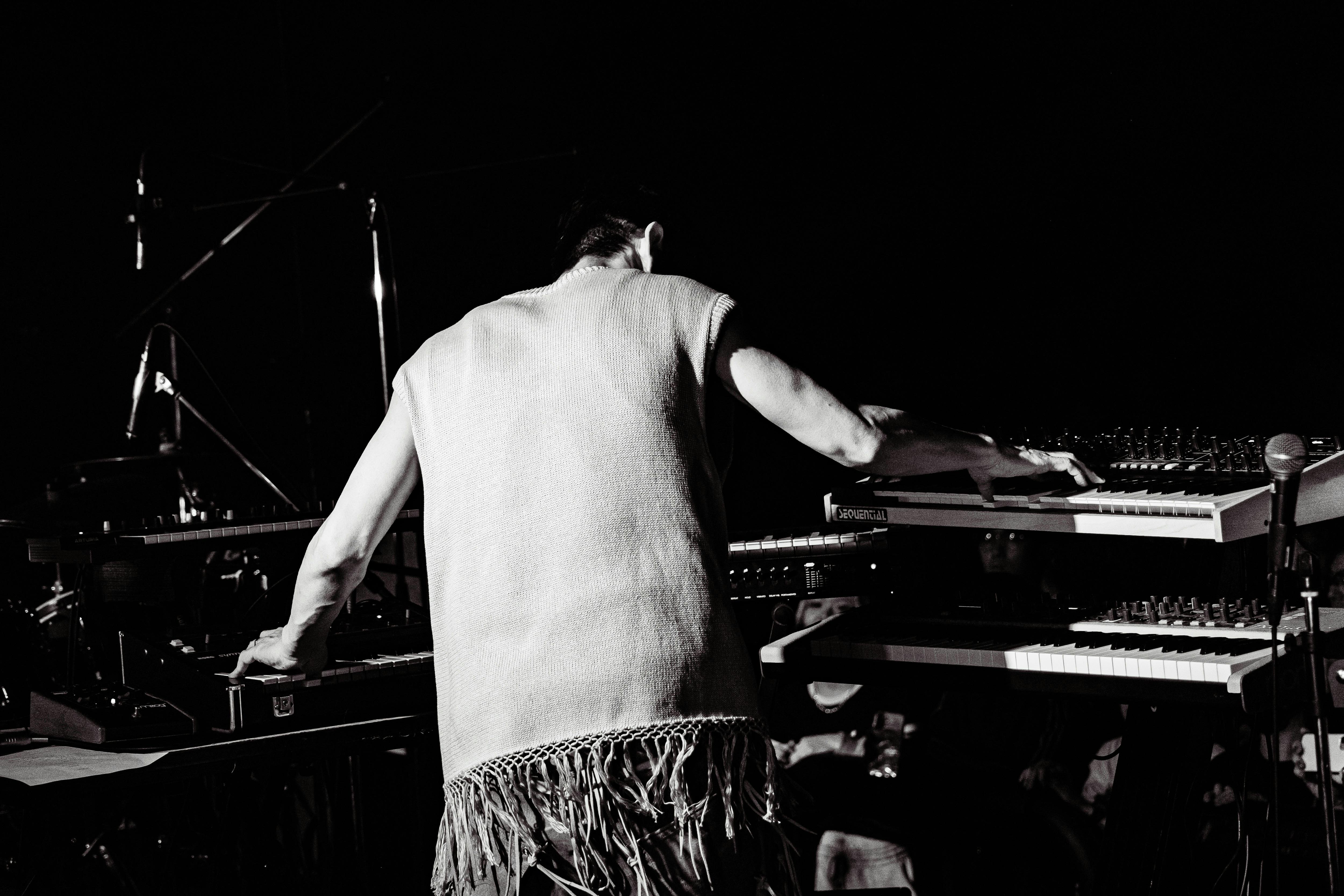black and white image of a man playing keyboard and mixing live taken from behind.