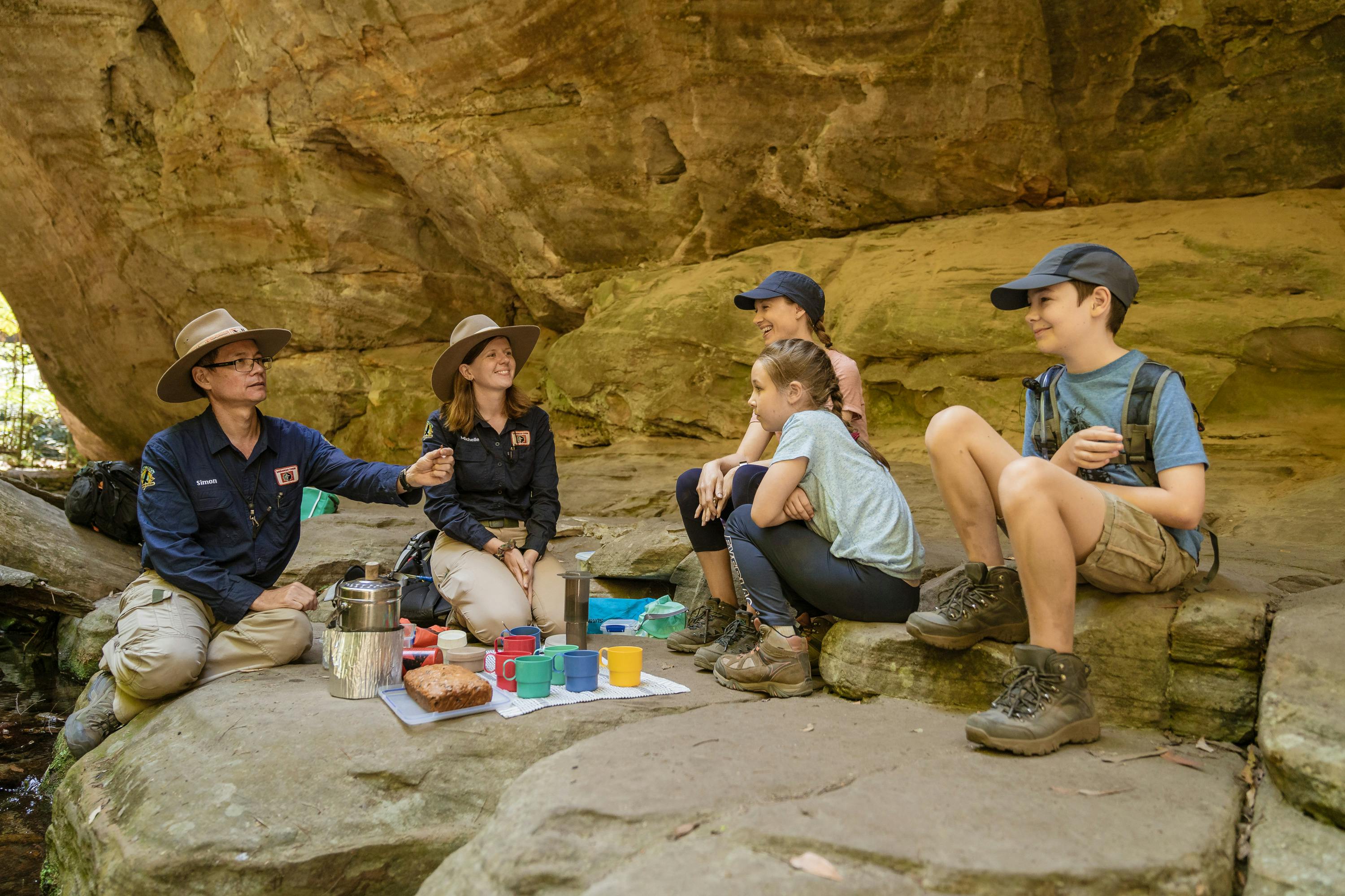 Two tour guides and a young family enjoy morning tea alongside a pretty creek at Carnarvon Gorge.