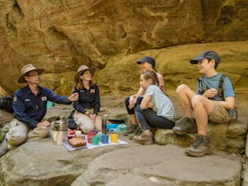 Two tour guides and a young family enjoy morning tea alongside a pretty creek at Carnarvon Gorge.