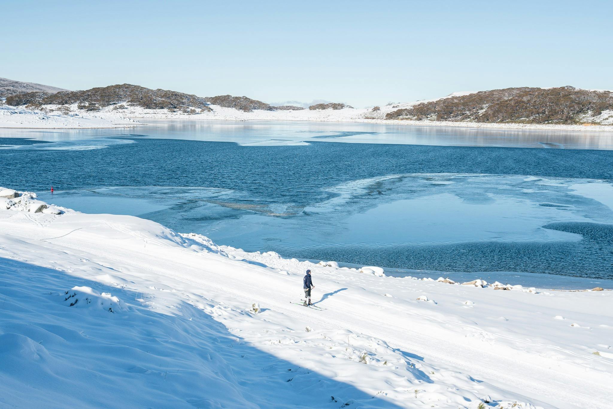 A lone skier takes in the tranquility of Rocky Valley Lake on a sunny day after fresh snowfall.
