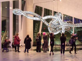people look at a hanging mechanical sculpture in a gallery