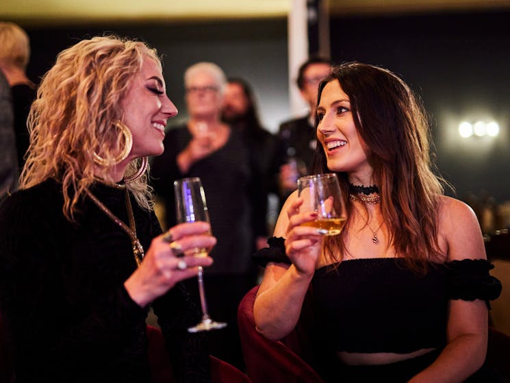 Two lovely ladies enjoy sparkling wine and laugh together in a busy bar.