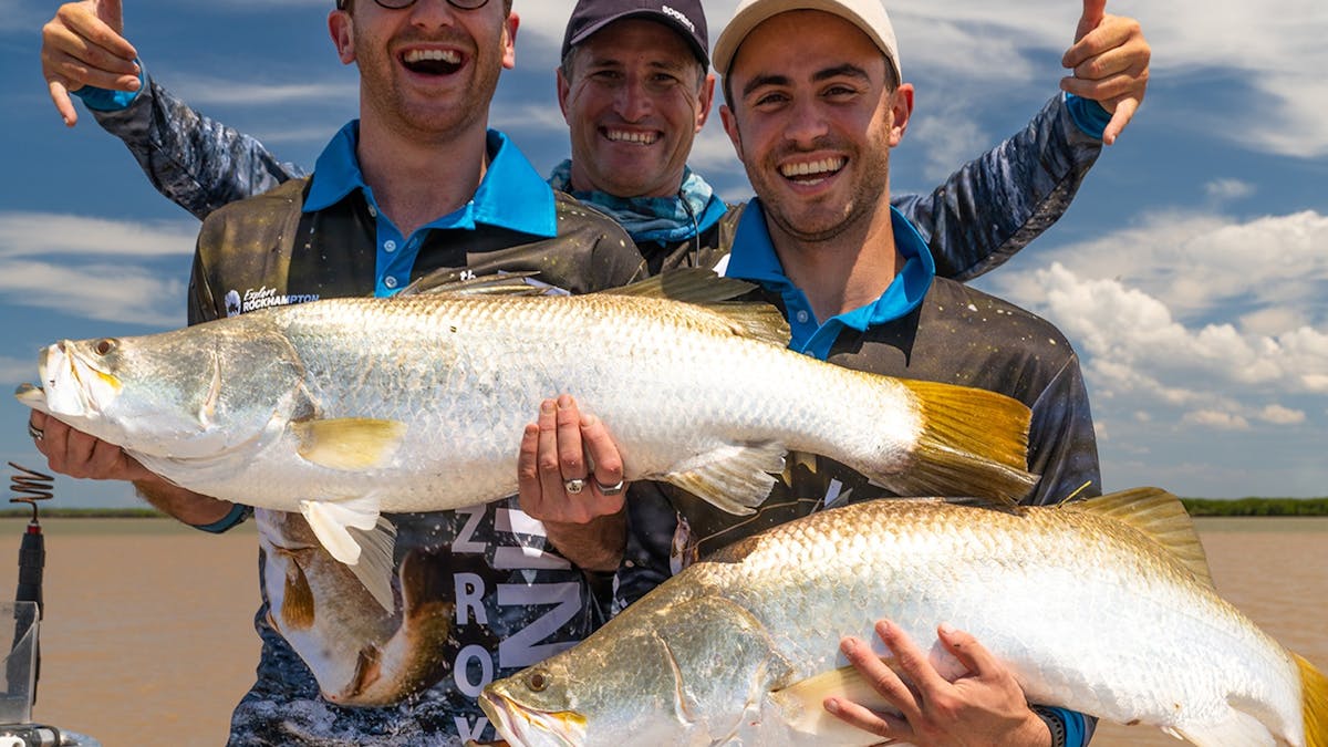 Three happy fishermen holding two giant barramundi fish in the Fitzroy River.