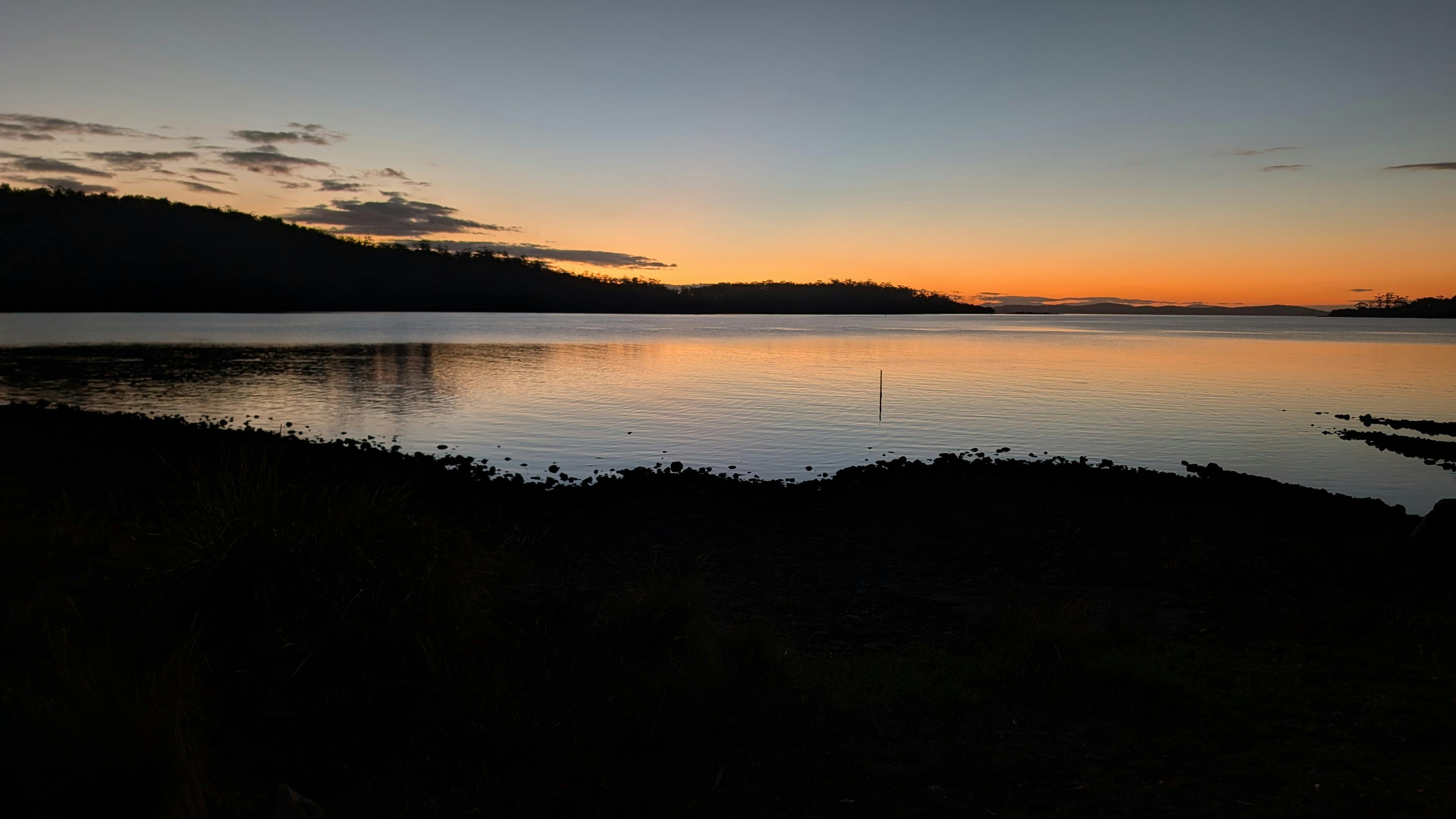 Sunset over calm Little Norfolk Bay with silhouetted shoreline and hills.