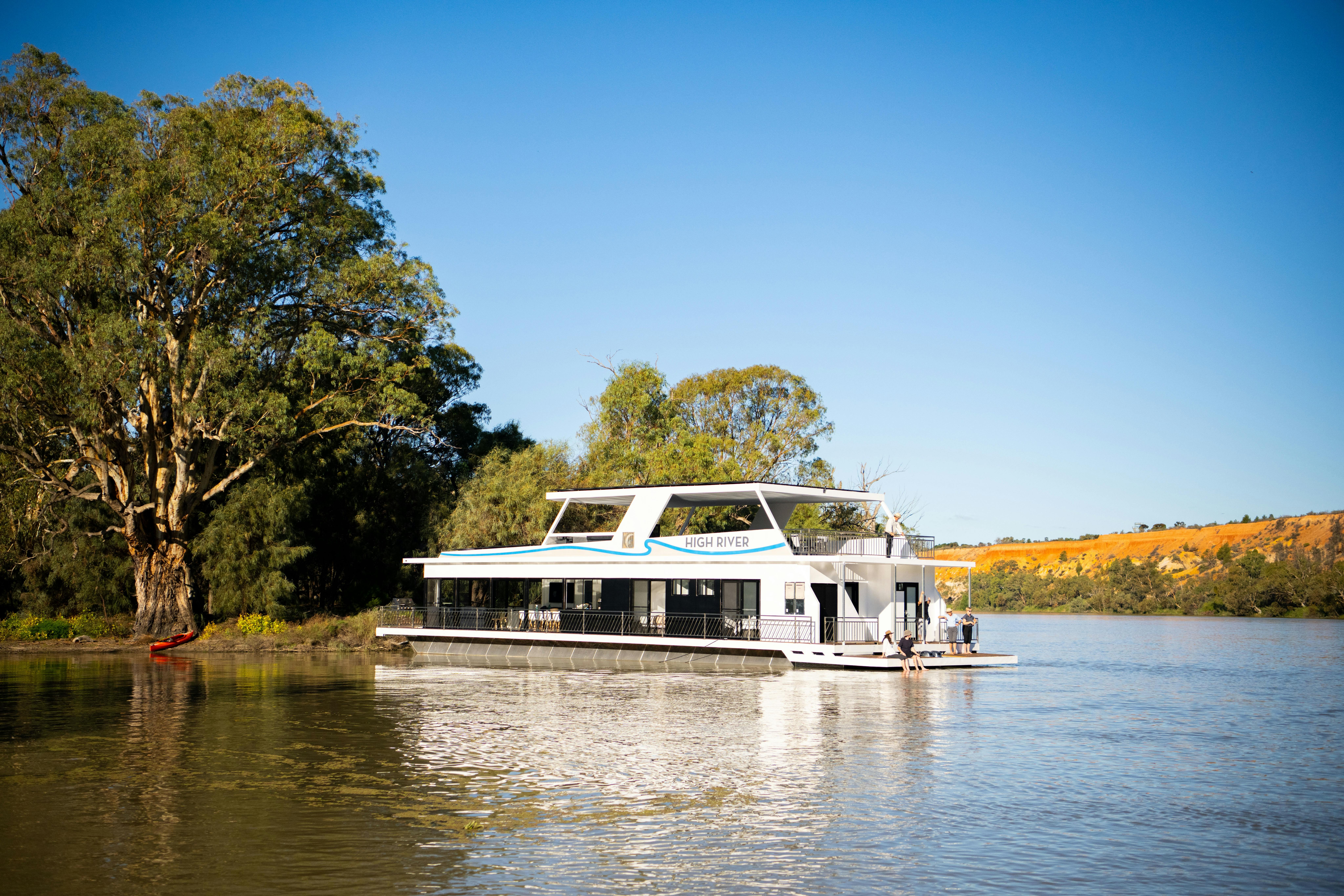 A houseboat on the Murray River with people sitting on the back deck