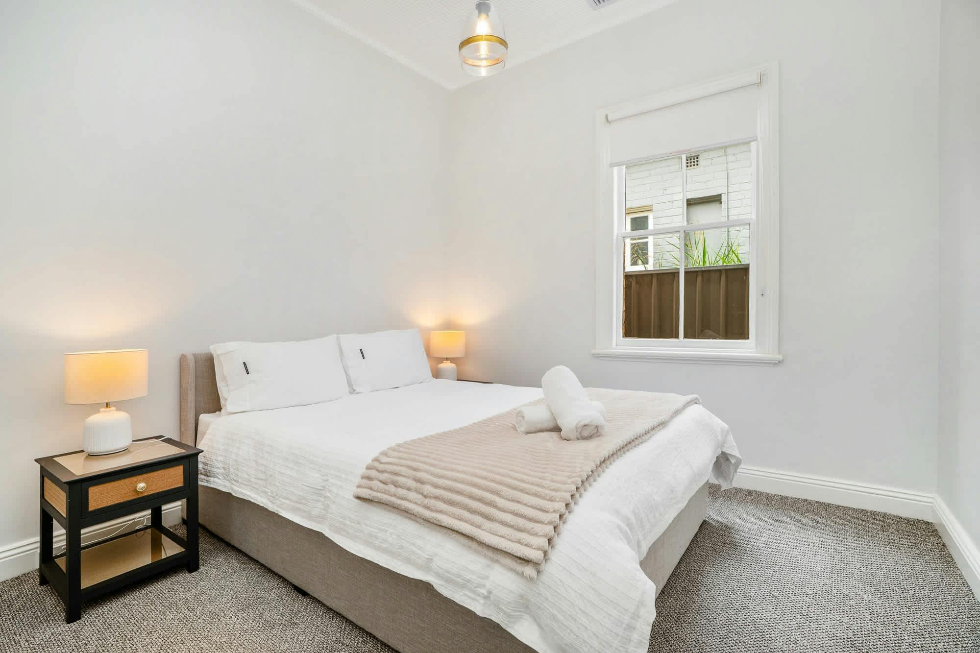 Bedroom with queen bed and window on the side of the home.