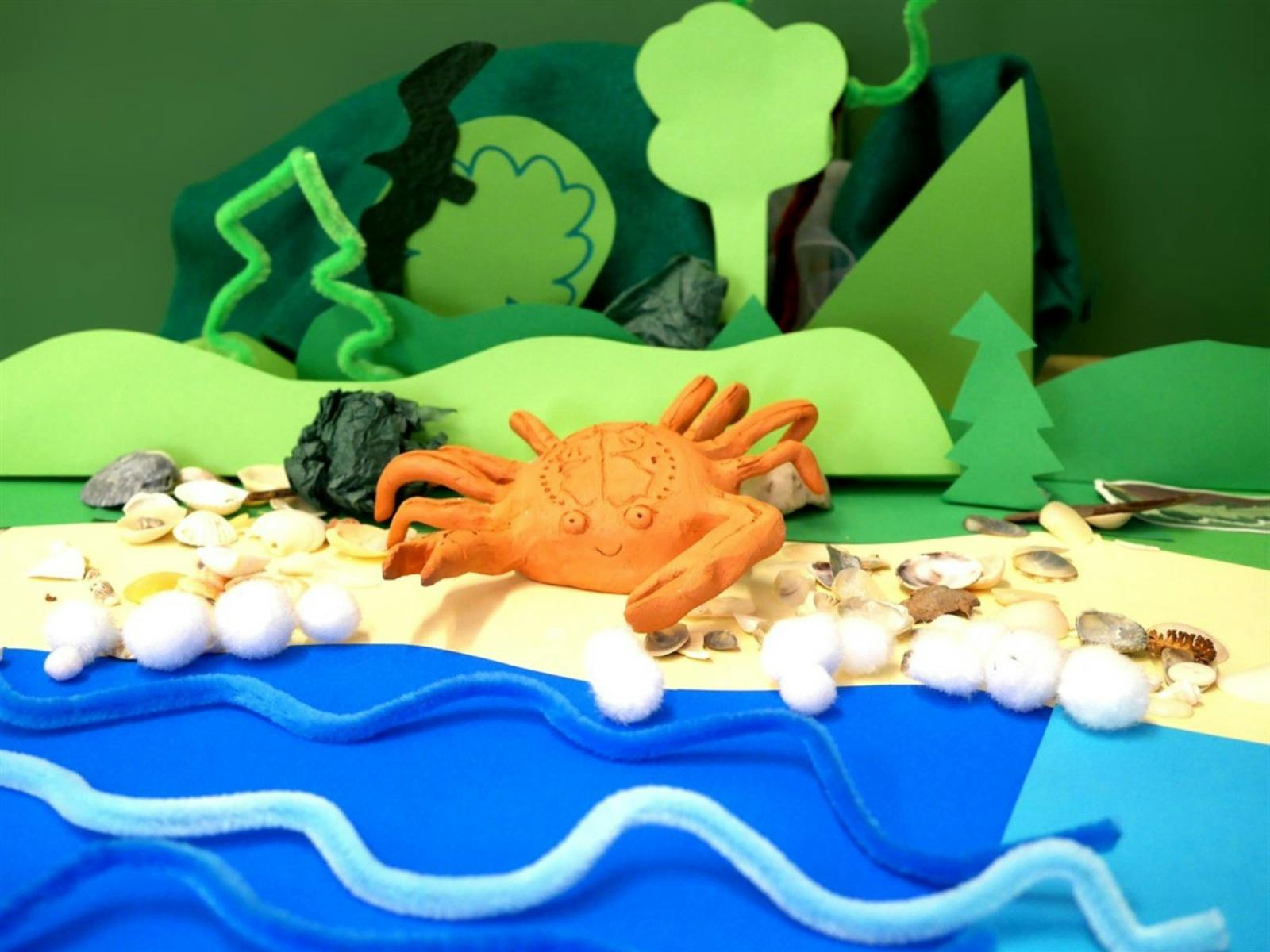 Orange crab figurine placed in an ocean made of blue paper and shells scattered on the floor.