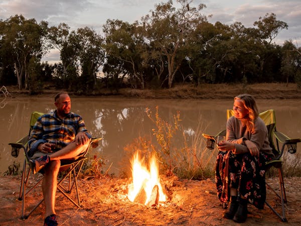 Two people sitting on campchairs, a campfire between them Two people sitting on campchairs, a campfire between them