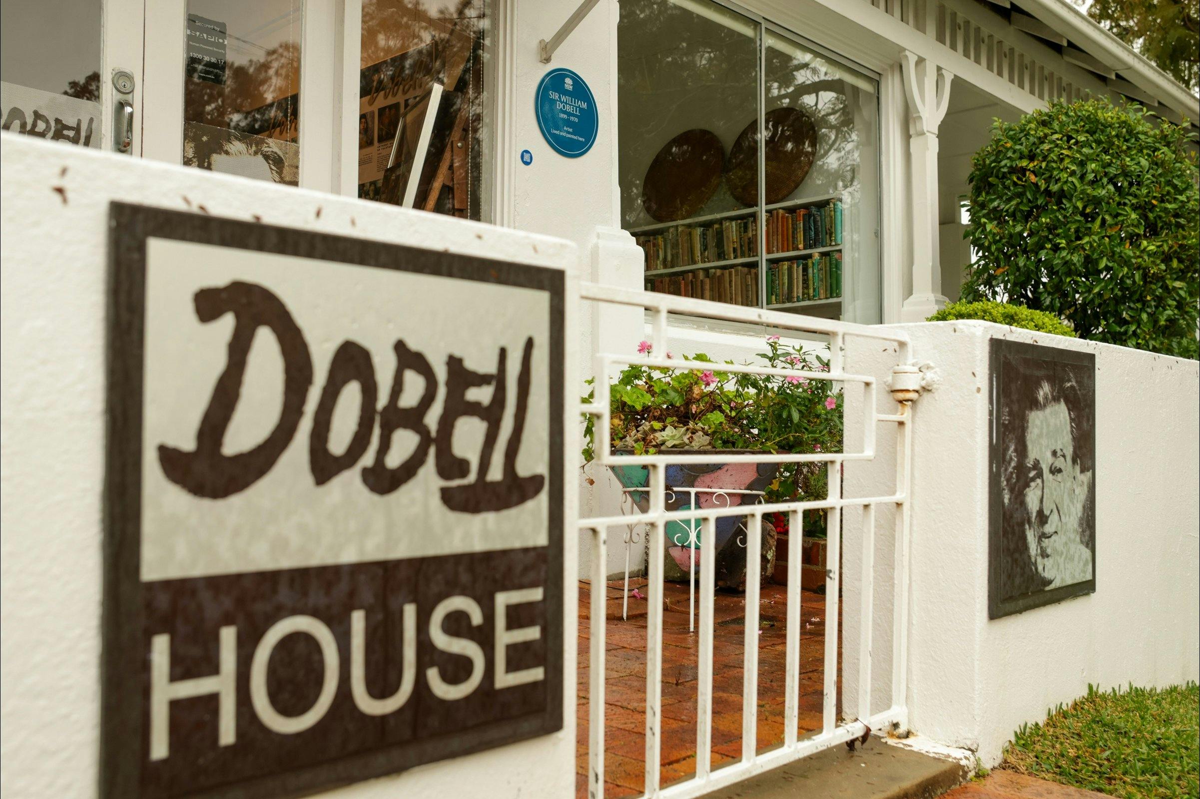 The front of Dobell House property with sign on fence, gate to front door, blue plaque on wall
