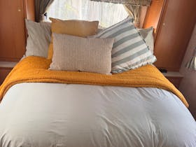 Comfortable double bed with multiple pillows and throw rug