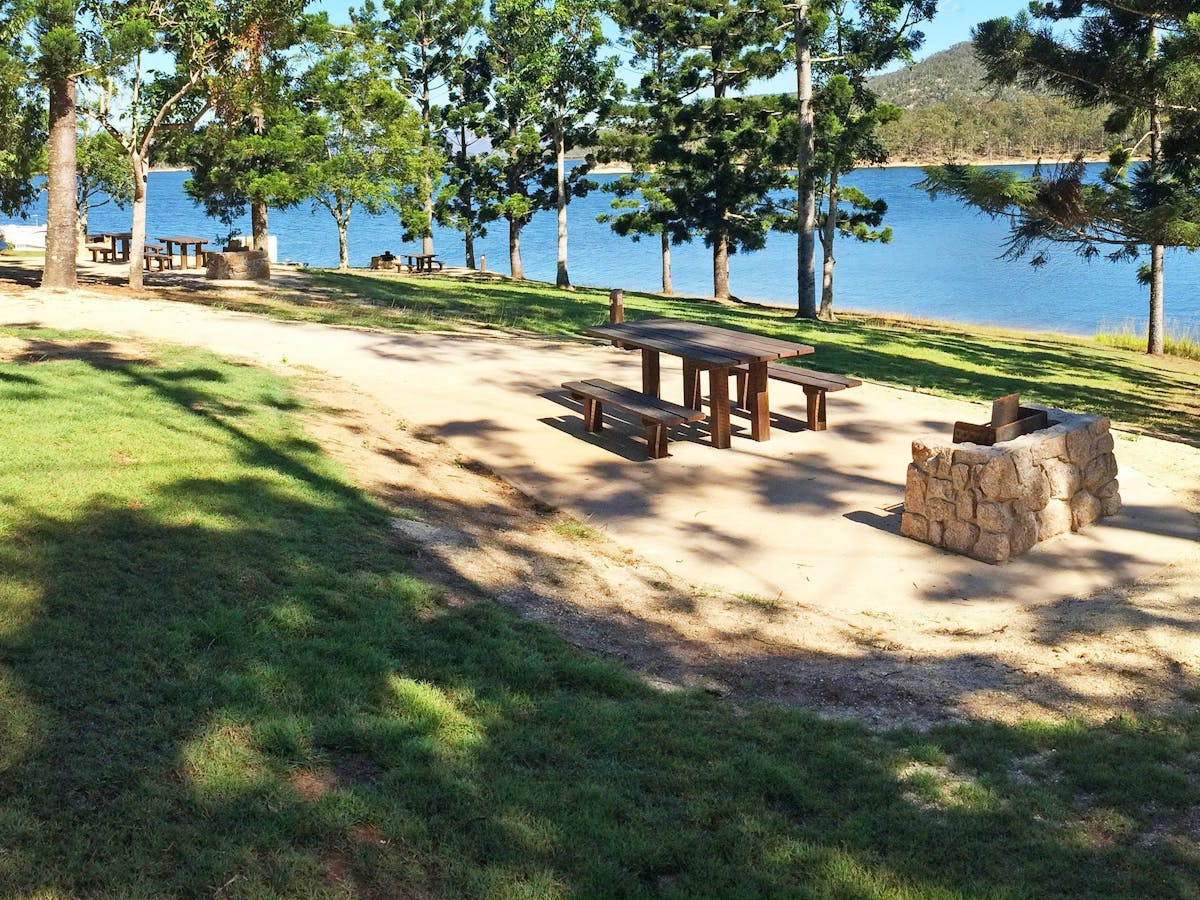 Picnic tables and wood-fired barbeque under hoop pines beside Lake Tinaroo.