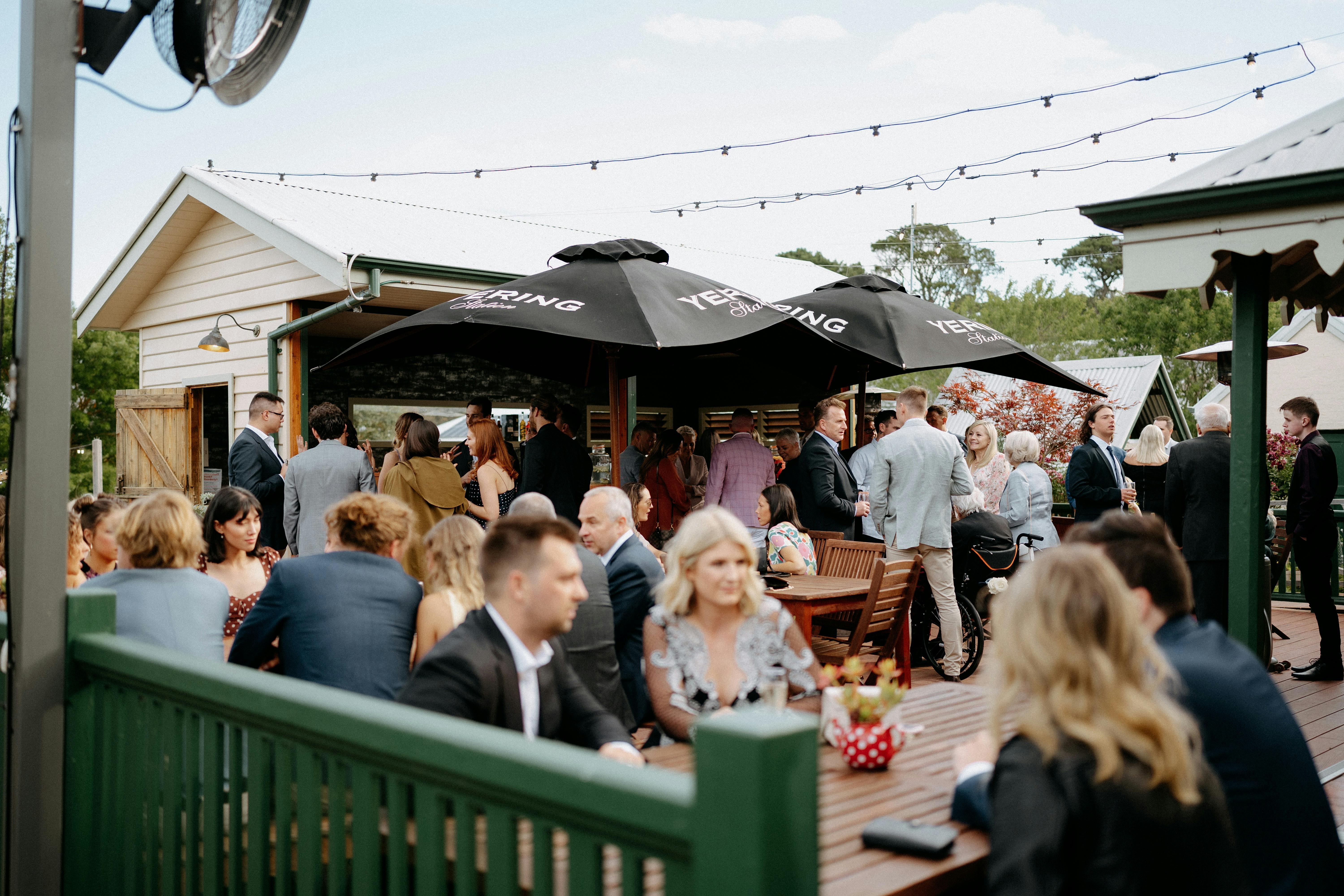 Outdoor gathering on a deck with people socialising under large umbrellas.