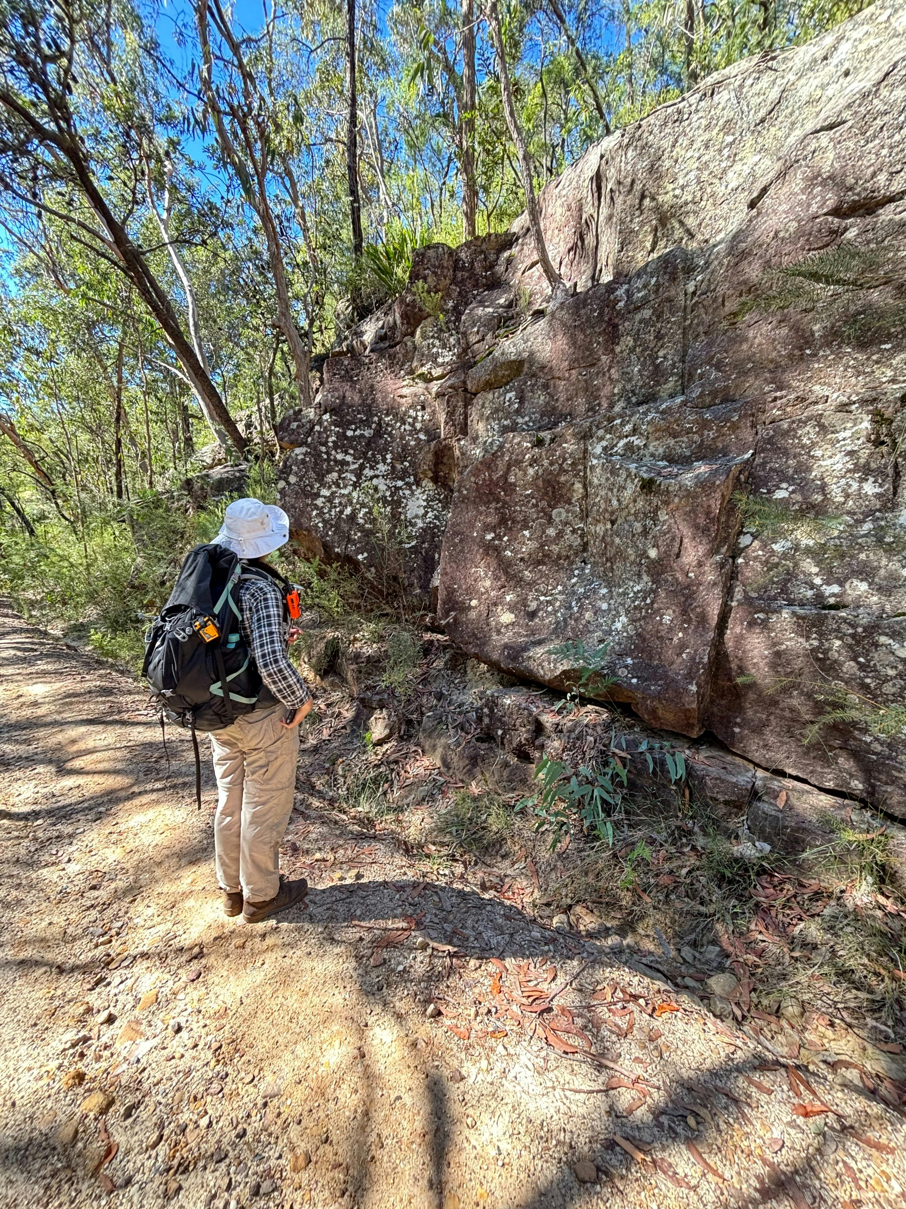 A woman standing in front of a rock wall that carries the marks of convict stone masons