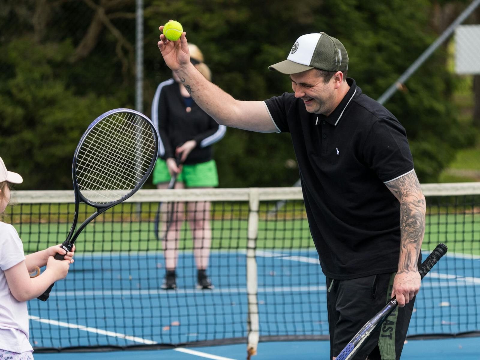 Father smiling as he shows his young daughter how to hit a tennis ball on our tennis courts