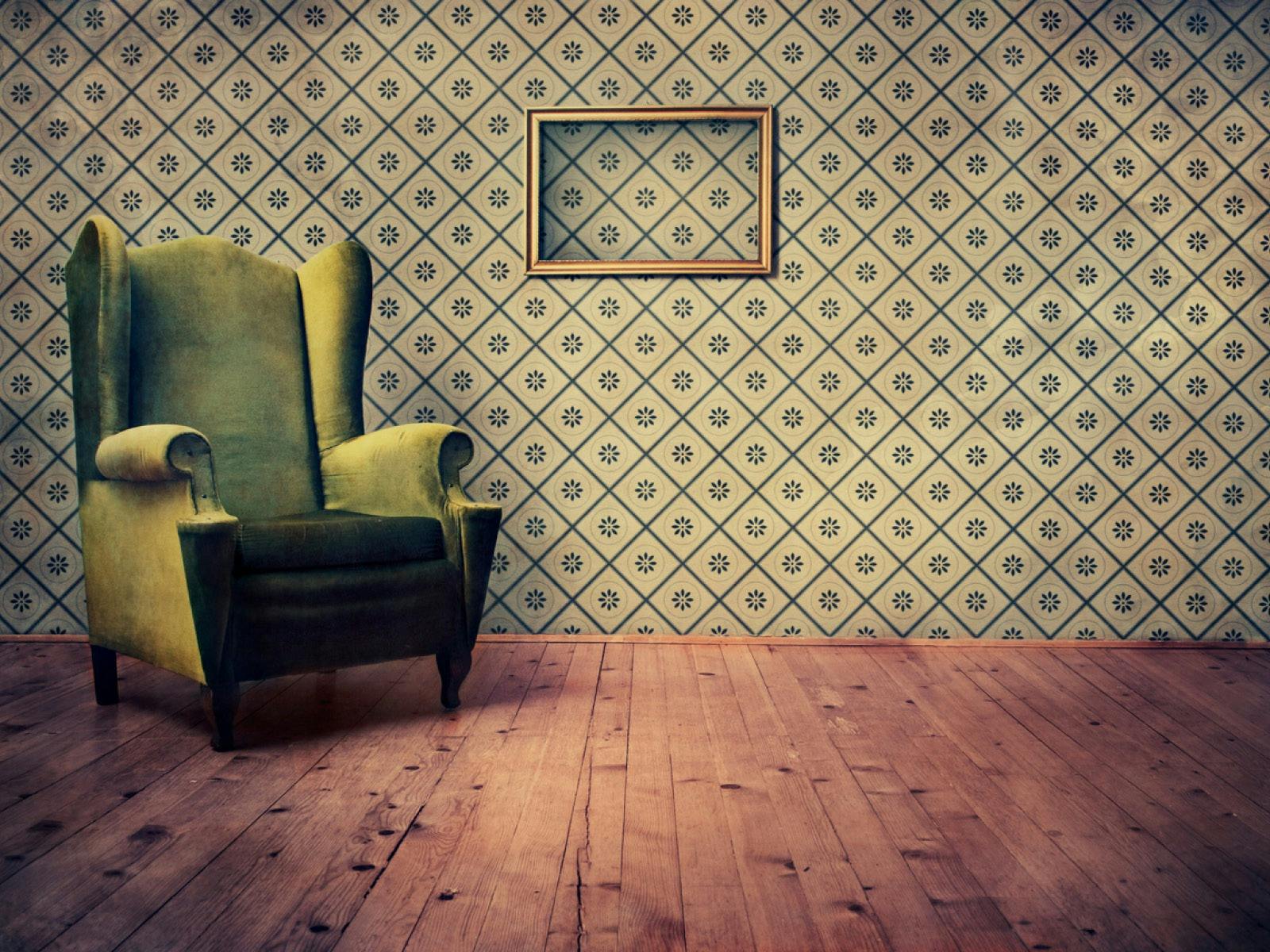 A green velvet armchair in corner of stark wallpapered  room, sitting on bare timber floor