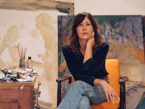 Amber sits in her studio with several paintings behind her